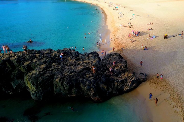Aerial view of Waimea Bay with sandy beach, blue water and the large shoreline rock